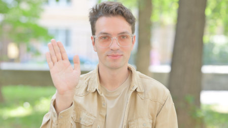 Outdoor Portrait of Waving Casual Young Man Saying Helloの写真素材