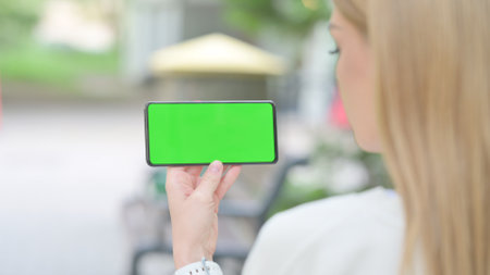 Woman Horizontally Holding Smartphone with Green Screen Outdoorの写真素材