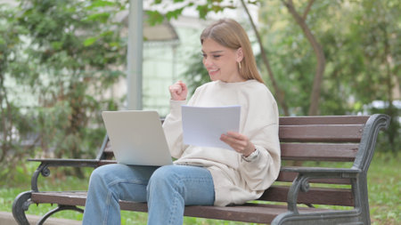 Casual Young Woman Celebrating while Using Laptop and Documents Outdoorの写真素材