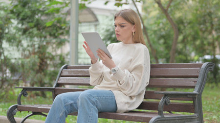 Young Woman with Loss on Tablet while Sitting Outdoor on a Benchの写真素材