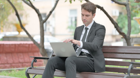 Businessman Leaving Bench Outdoor after Working on Laptopの写真素材