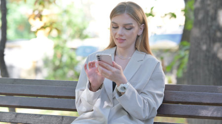 Young Businesswoman using Phone while Sitting on Benchの写真素材