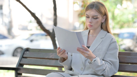 Young Businesswoman Reading Documents while Sitting on Benchの写真素材