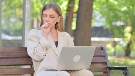 Coughing Young Businesswoman Using Laptop Outdoorの写真素材
