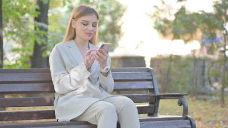 Young Business Lady using Phone while Sitting on Benchの写真素材