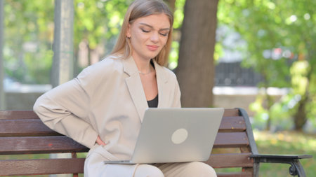 Young Businesswoman Using Laptop with Back Pain while Sitting on Benchの写真素材