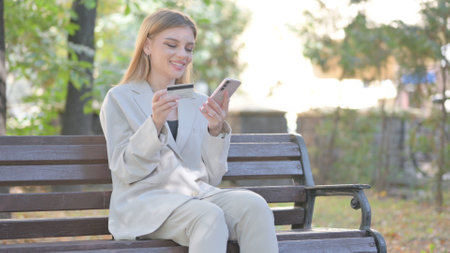 Young Business Lady Shopping Online while Sitting on Benchの写真素材