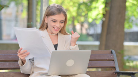 Young Businesswoman Celebrating while Using Laptop and Documents Outdoorの写真素材