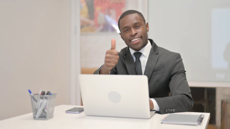 Thumbs Up by African Businessman on Laptop in Officeの写真素材