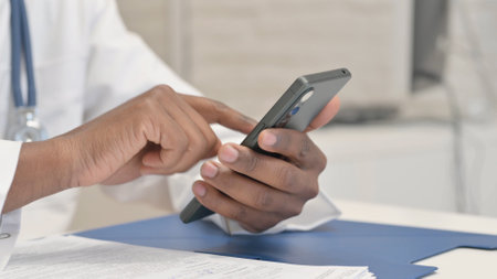 Close up of African Doctor Browsing Internet on Smartphoneの写真素材