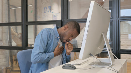 Coughing African Businessman while Working on Computerの写真素材