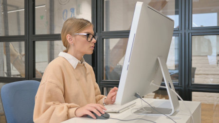 Woman in Glasses Working on Desktop in Officeの写真素材