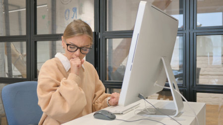 Woman in Glasses Coughing while Working on Computerの写真素材