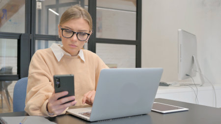Female Worker Working on Laptop and Using Smartphoneの写真素材