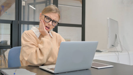 Female Worker with Toothache Working on Laptop in Officeの写真素材