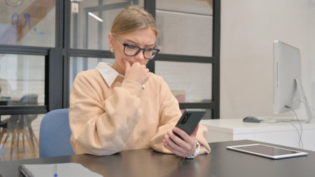 Female Worker Shocked by Loss on Phone in Officeの写真素材