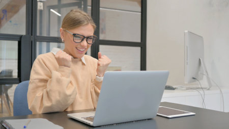 Excited Female Worker Celebrating Success on Laptop in Officeの写真素材
