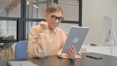 Female Worker Celebrating Success on Tablet in Officeの写真素材