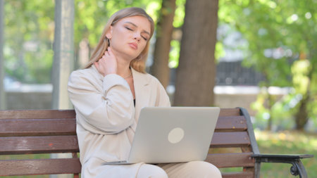 Young Businesswoman with Neck Pain Working on Laptop Outdoorの写真素材
