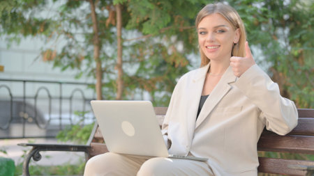 Thumbs Up by Young Business Lady on Laptop Outdoorの写真素材