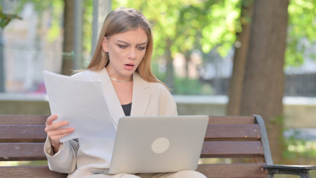 Young Businesswoman Feeling Upset while Reading Contract and Using Laptop Outdoorの写真素材