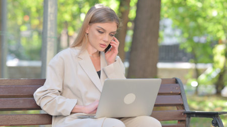 Young Businesswoman Talking on Phone and Using Laptop Outdoorの写真素材