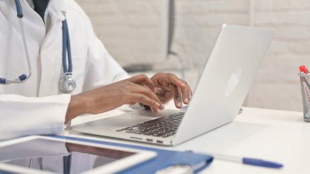 Close up of African Doctor Typing on Laptop in Hospitalの写真素材