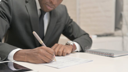 Close Up of African Businessman Writing Documentsの写真素材