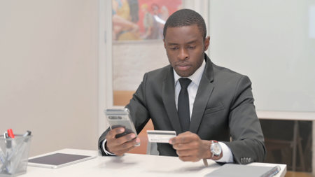 African Businessman using Smartphone and Credit Card at Work in Officeの写真素材