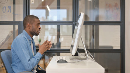 African Businessman Doing Online Video Chat on Desktop in Officeの写真素材
