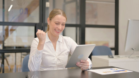 Mature Business Woman Celebrating Success on Tablet in Officeの写真素材
