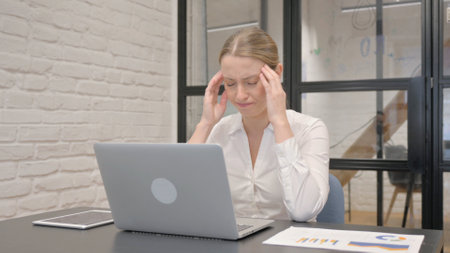 Middle Aged Business Woman with Headache Working on Laptopの写真素材