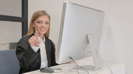 Business Woman Pointing at Camera while Working on Desktopの写真素材