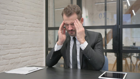 Middle Aged Businessman with Headache Sitting at Workの写真素材