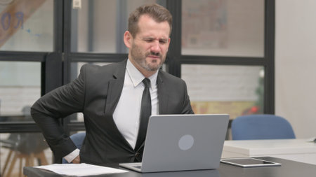 Businessman with backache Working on Laptopの写真素材