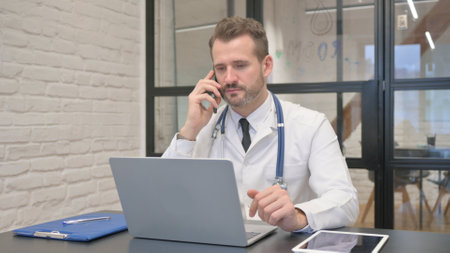 Middle Aged Doctor Talking on Phone in Clinicの写真素材