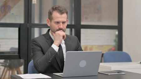 Brainstorming Businessman Working on Laptop in Officeの写真素材