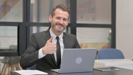 Thumbs Up by Businessman While Working on Laptopの写真素材