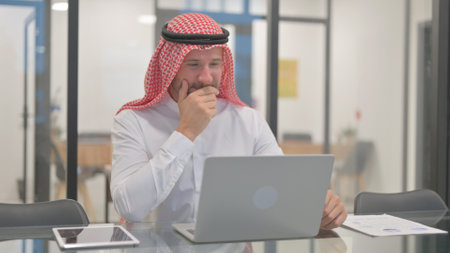 Excited Arab Man Celebrating Success on Laptop in Officeの写真素材