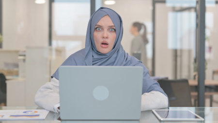 Shocked Arab Woman Looking at Camera while Working on Laptopの写真素材