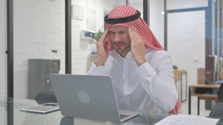 Middle Aged Muslim Man with Migraine Working in Officeの写真素材