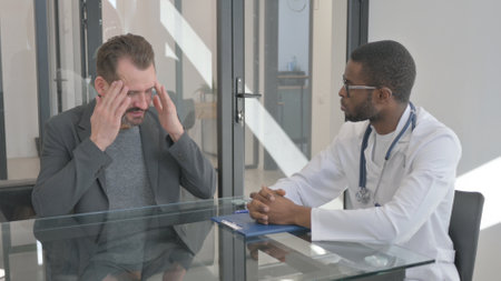 Middle Aged Man with Headache Talking with Doctorの写真素材