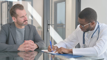 Doctor Discussing Treatment with Patient and Writing Medicineの写真素材