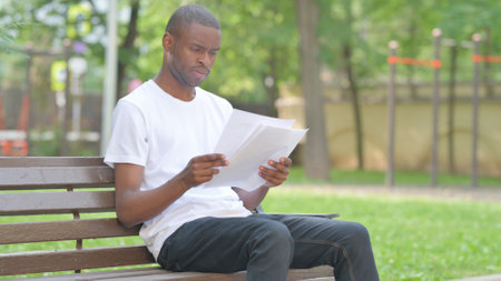 Outdoor Sitting Young African Man Reading Documentsの写真素材