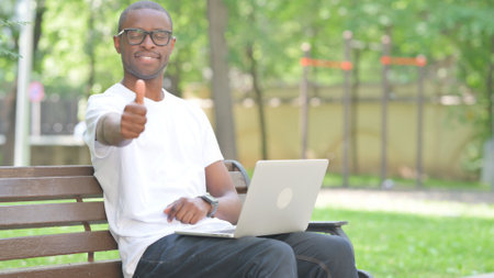 Thumbs Up by Young African Man Using Laptop Outdoorの写真素材
