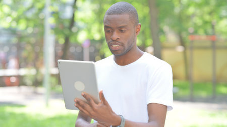 Portrait of African Man Doing Video Chat on Tablet Outdoor in Parkの写真素材