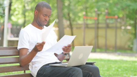 Young African Man Working on Documents and Laptop Outdoorの写真素材