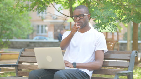 African American Man with Laptop Pointing at Camera while Sitting Outdoorの写真素材