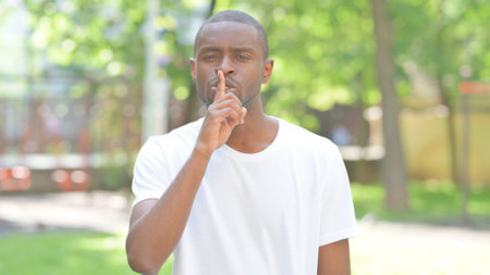 Young African Man with Finger on Lips Outdoor in Parkの写真素材