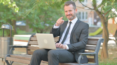 Young Businessman Pointing at Camera while Using Laptopの写真素材